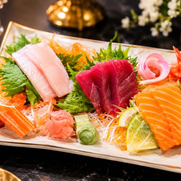 Assorted sashimi platter with tuna, salmon, hamachi, crab sticks, and shrimp, garnished with ginger and wasabi.