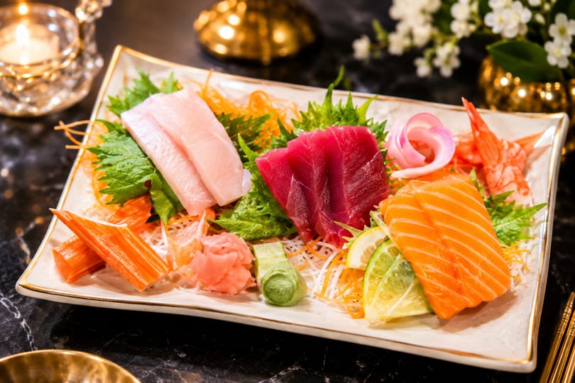 Assorted sashimi platter with tuna, salmon, hamachi, crab sticks, and shrimp, garnished with ginger and wasabi.