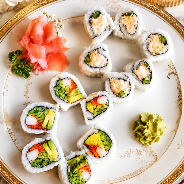 Two types of sushi rolls, pickled ginger, and wasabi elegantly arranged on a white and gold plate.