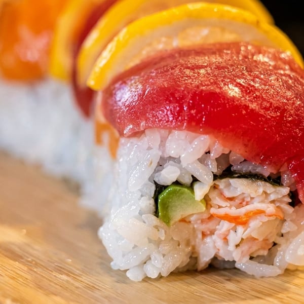 Close-up of a sushi roll with tuna, crab, avocado, and lemon slices on a wooden board.