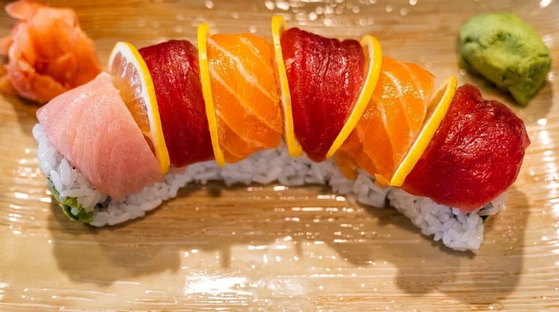 Rainbow sushi roll with tuna, salmon, and lemon slices, served with ginger and wasabi.